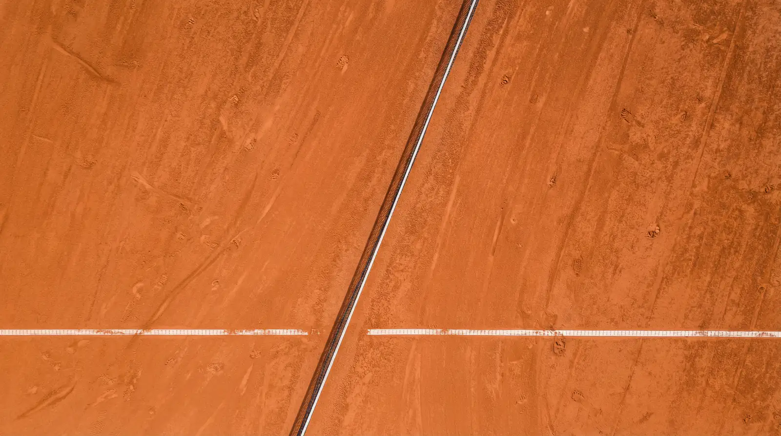Vista cenital de una pista de tierra batida con líneas blancas marcadas y red central